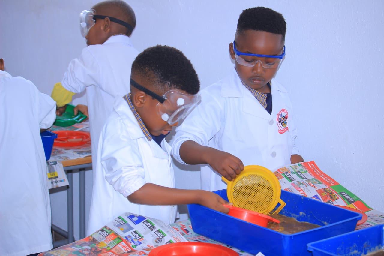 Learners in lab coats and goggles sifting materials during a science experiment