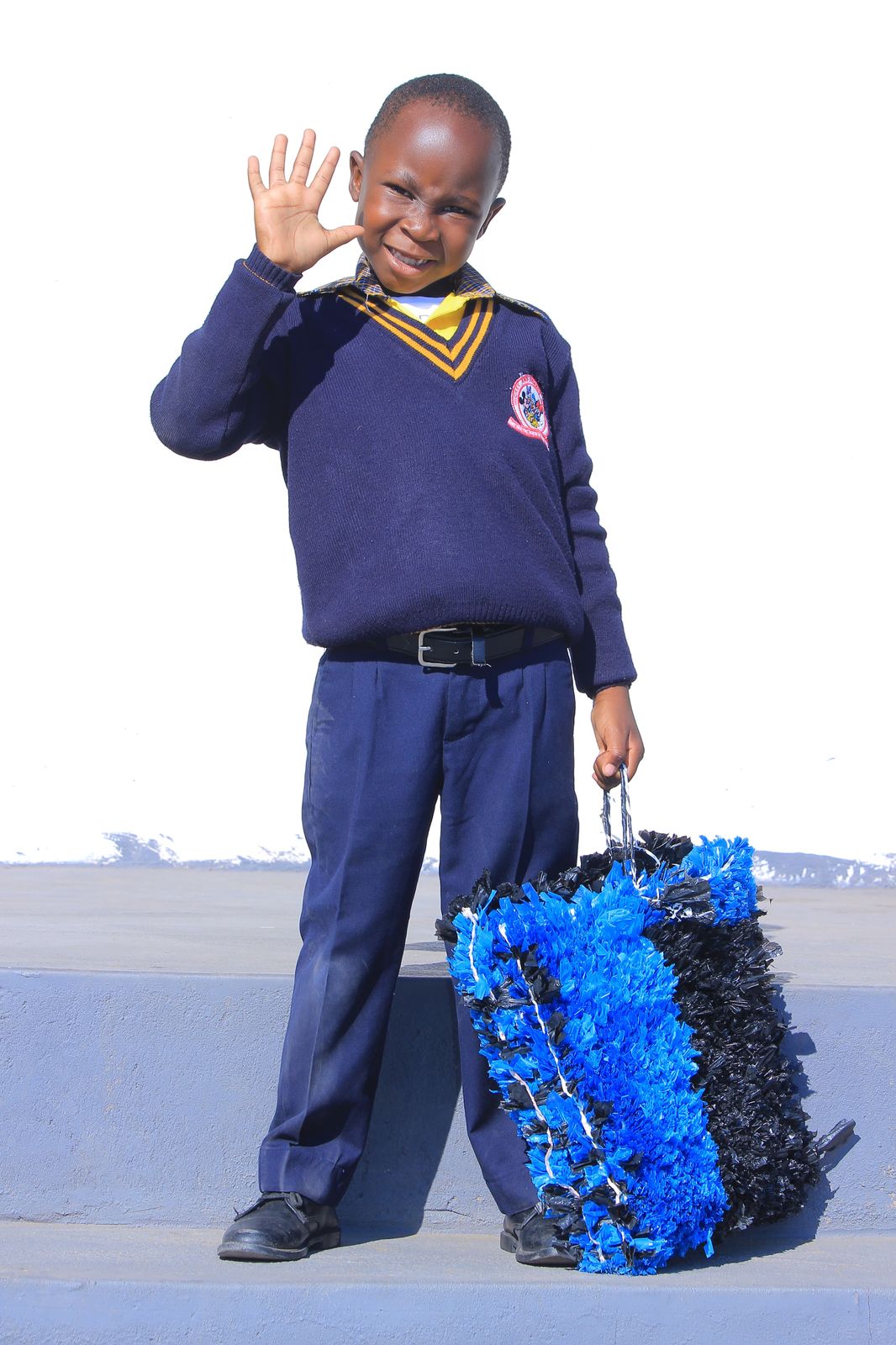 Learner waving beside a bright blue woven plastic bag