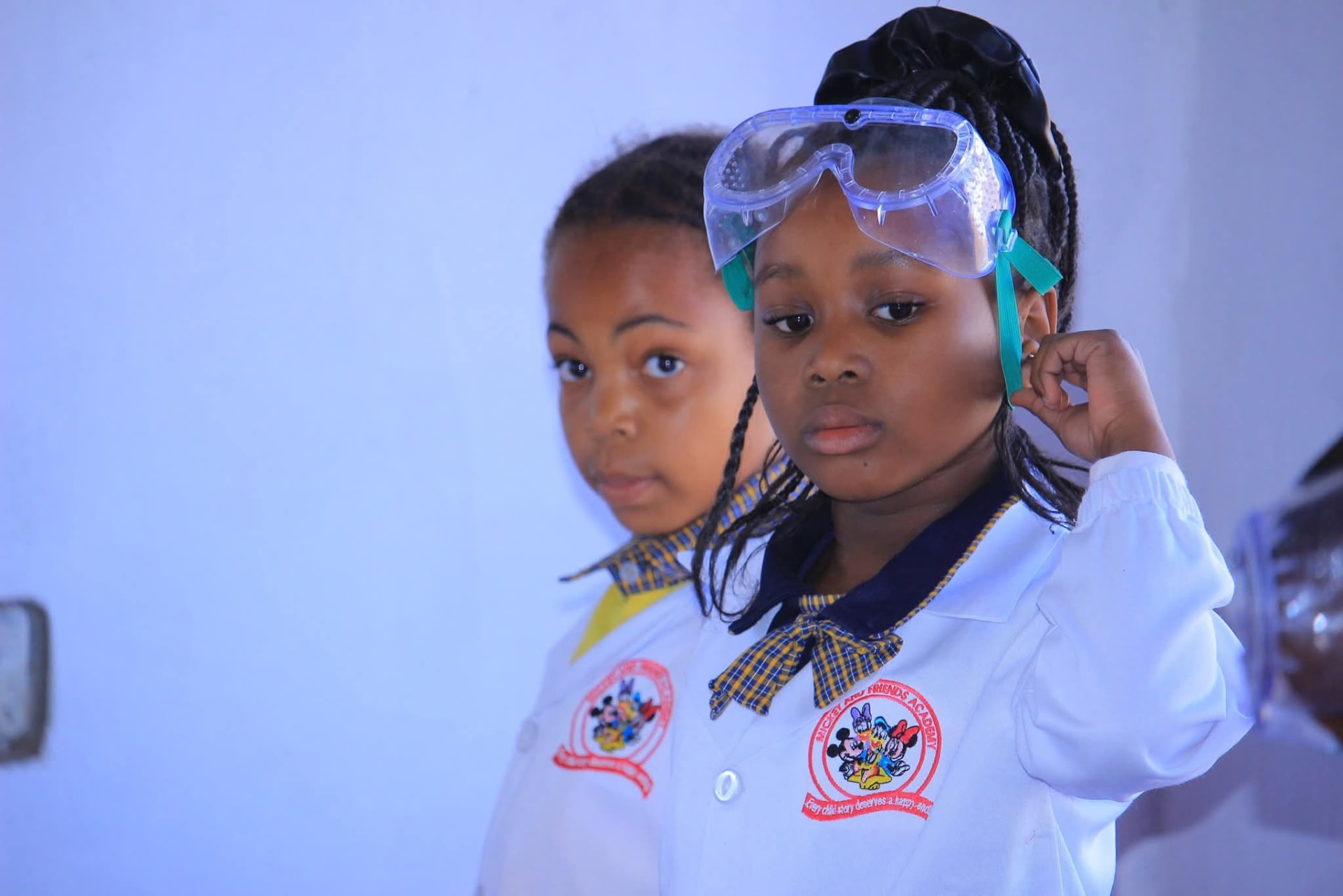 Two learners in Mickey and Friends Academy lab coats and safety goggles