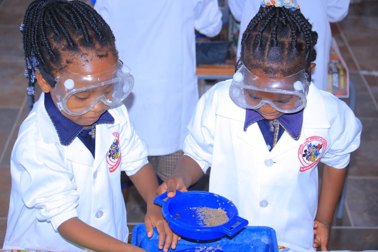 Two young girls in goggles and lab coats sieving samples