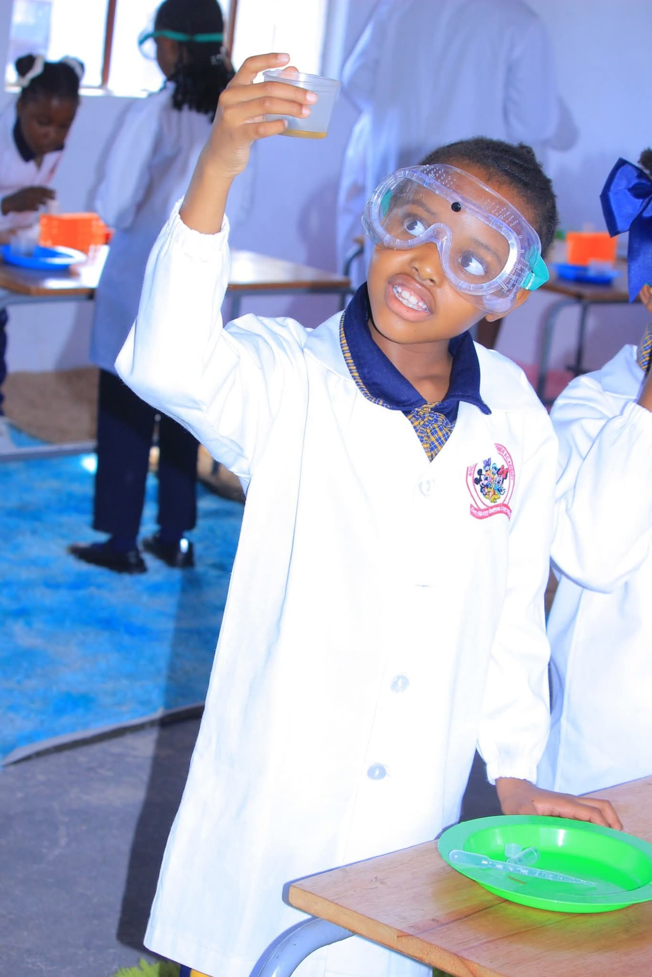 Girl in goggles holding up a sample cup during a chemistry lesson