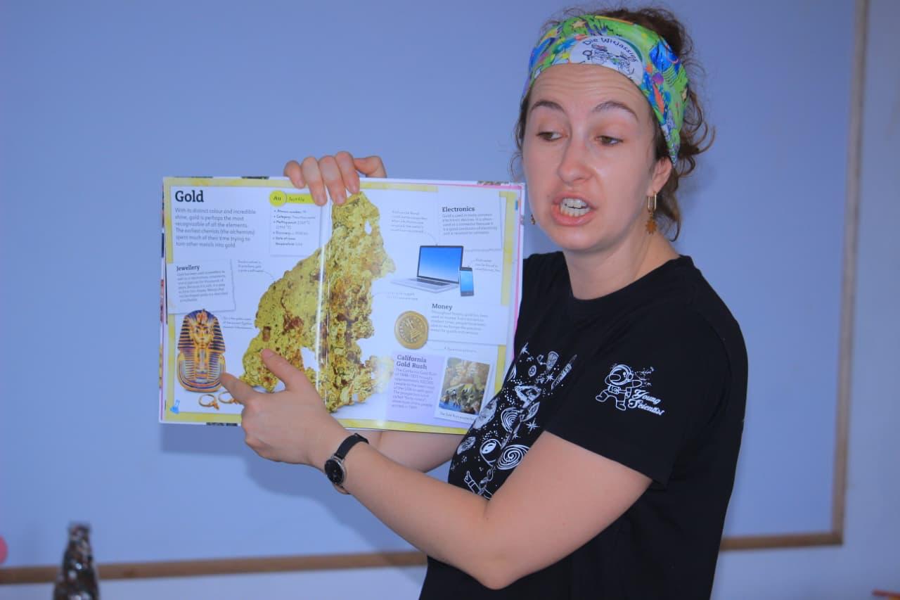 Science facilitator showing a book page about gold to the class